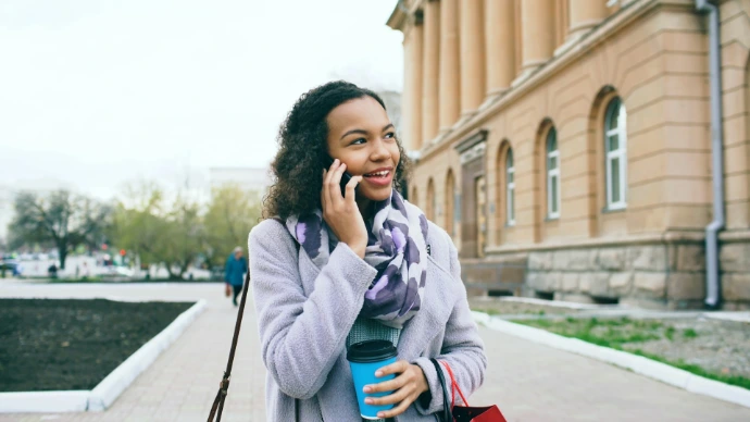 A woman talking on the phone and holding coffee.